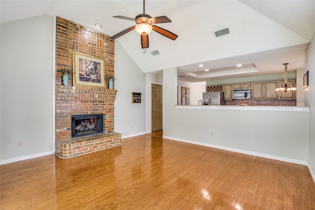 unfurnished living room featuring ceiling fan with notable chandelier, a fireplace, light wood-type flooring, and brick wall