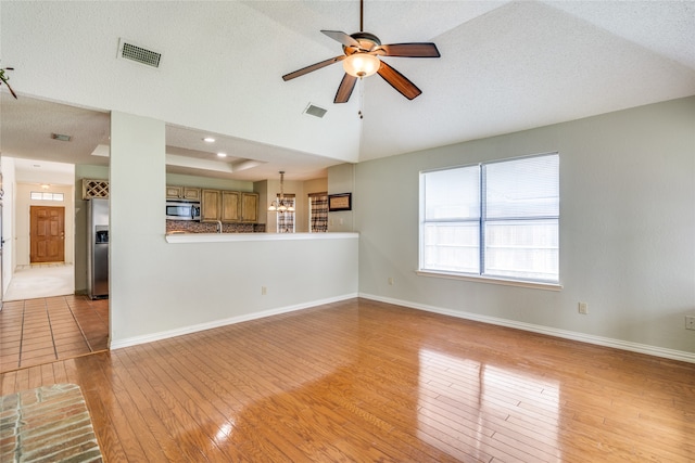 unfurnished living room with light tile patterned flooring, a textured ceiling, ceiling fan with notable chandelier, and a raised ceiling