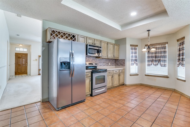 kitchen featuring appliances with stainless steel finishes, a tray ceiling, light tile patterned floors, and decorative backsplash