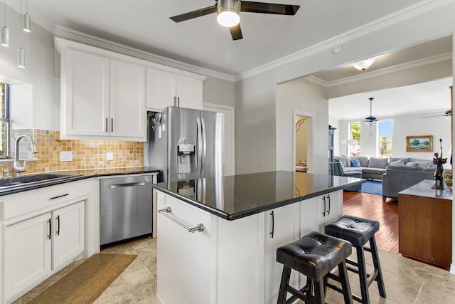 kitchen featuring appliances with stainless steel finishes, white cabinets, a center island, ornamental molding, and sink