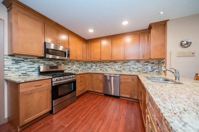 kitchen with light stone countertops, dark wood-type flooring, tasteful backsplash, a sink, and stainless steel appliances