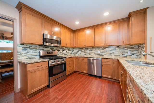 kitchen with light stone counters, a sink, dark wood finished floors, stainless steel appliances, and tasteful backsplash