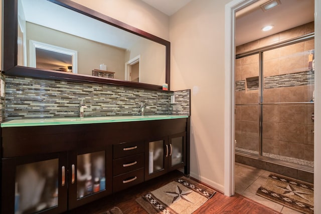 bathroom featuring decorative backsplash, double vanity, a shower stall, and a sink