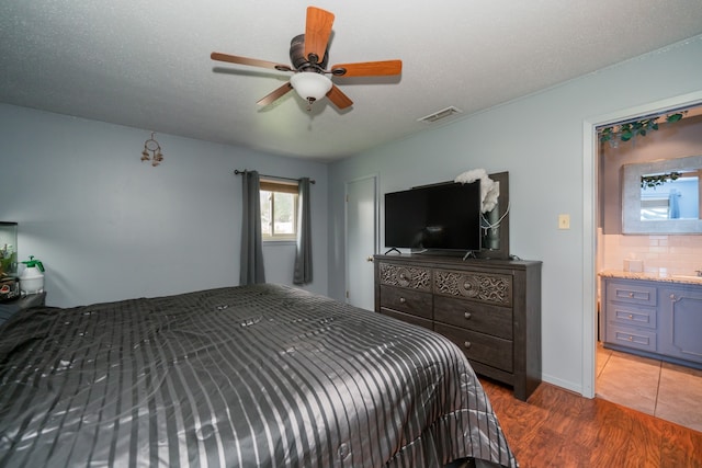 bedroom with ceiling fan, a textured ceiling, connected bathroom, and hardwood / wood-style flooring