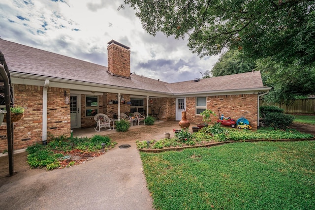 rear view of property with a shingled roof, a patio, a chimney, and brick siding