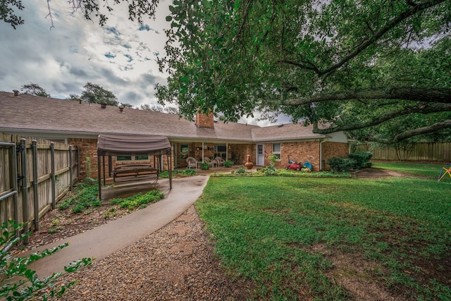 rear view of house with fence, a chimney, a lawn, and brick siding