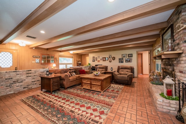 living room featuring a brick fireplace, beam ceiling, and wood walls