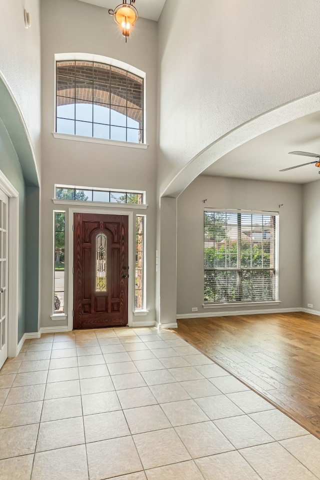 foyer entrance featuring light tile patterned floors, baseboards, a high ceiling, and ceiling fan