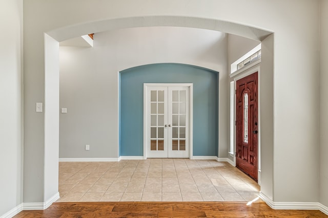 foyer with light tile patterned flooring, french doors, baseboards, and arched walkways