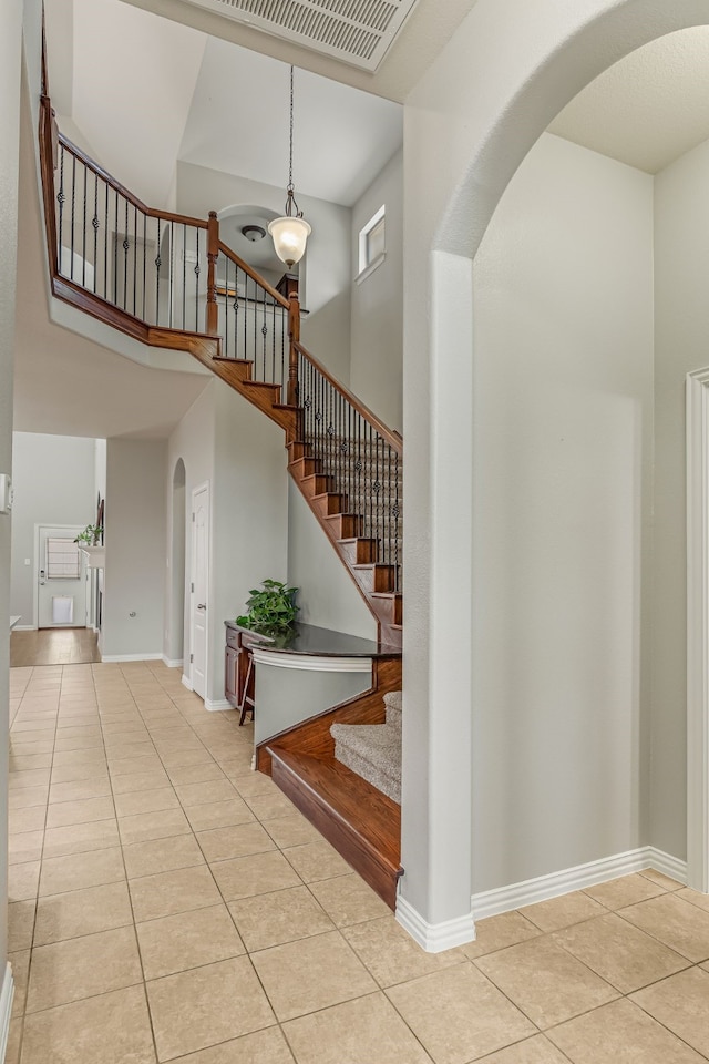 staircase featuring tile patterned floors, a high ceiling, baseboards, and arched walkways