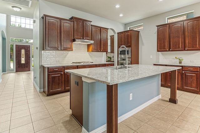 kitchen with visible vents, under cabinet range hood, arched walkways, appliances with stainless steel finishes, and light tile patterned flooring