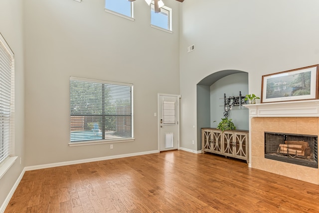 unfurnished living room with a ceiling fan, wood finished floors, visible vents, baseboards, and a tiled fireplace