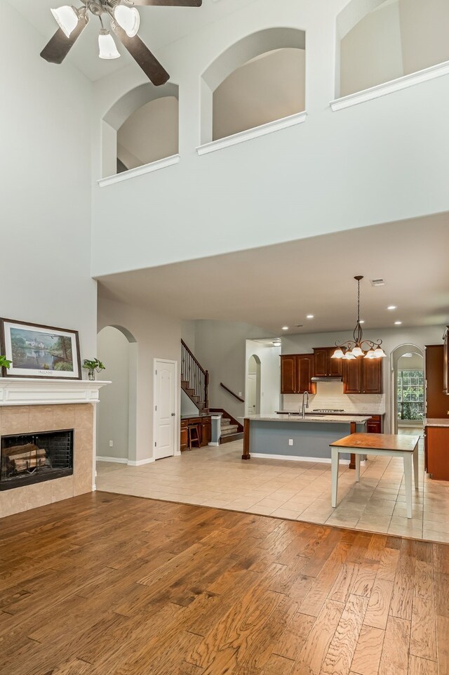 living room featuring a towering ceiling, stairway, light wood-style flooring, and a tiled fireplace