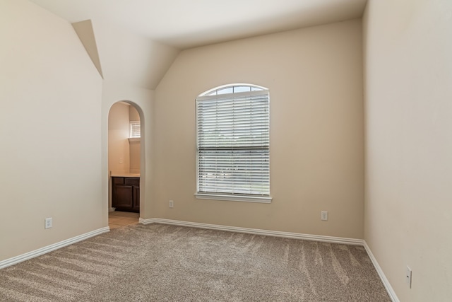 spare room with vaulted ceiling, arched walkways, baseboards, and light carpet