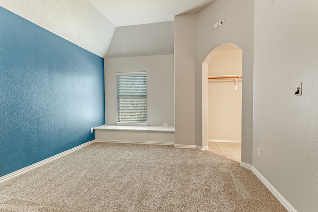 unfurnished bedroom with a walk in closet, arched walkways, carpet flooring, baseboards, and vaulted ceiling