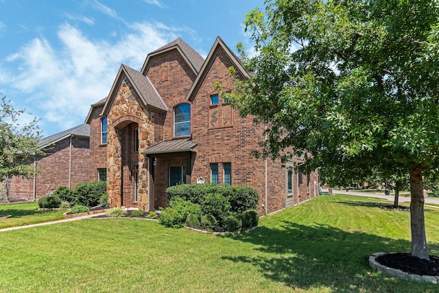 english style home featuring a standing seam roof, stone siding, a front yard, metal roof, and brick siding