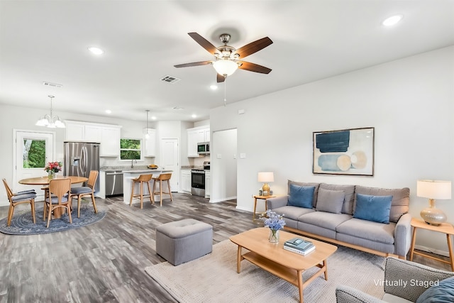 living room with ceiling fan with notable chandelier, sink, and dark wood-type flooring