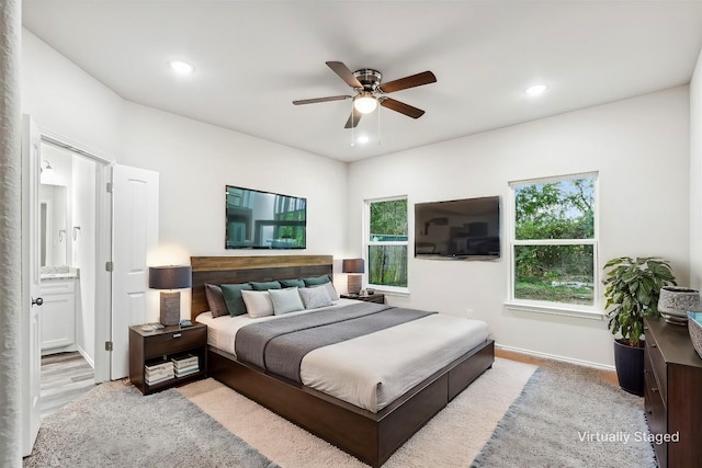 bedroom with light wood-type flooring, ensuite bathroom, multiple windows, and ceiling fan