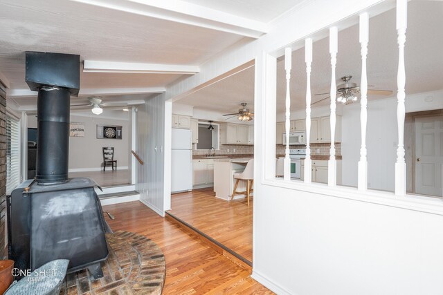 living room with beam ceiling, a wood stove, sink, a textured ceiling, and light wood-type flooring