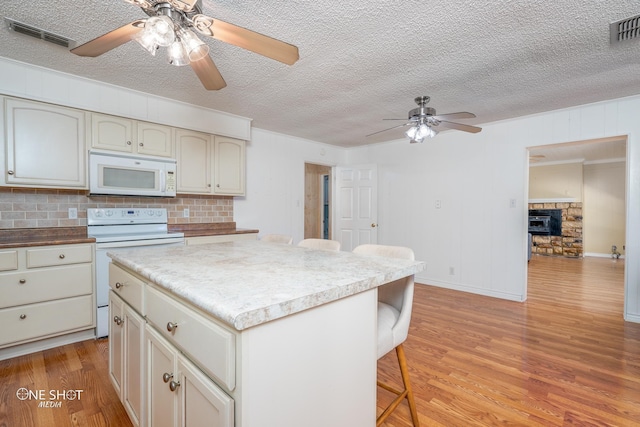 kitchen featuring a stone fireplace, a breakfast bar area, a kitchen island, white appliances, and light hardwood / wood-style floors