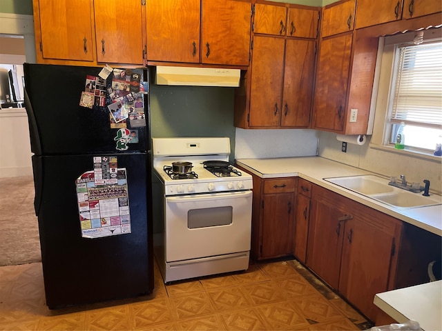 kitchen with white gas stove, sink, black fridge, and light carpet