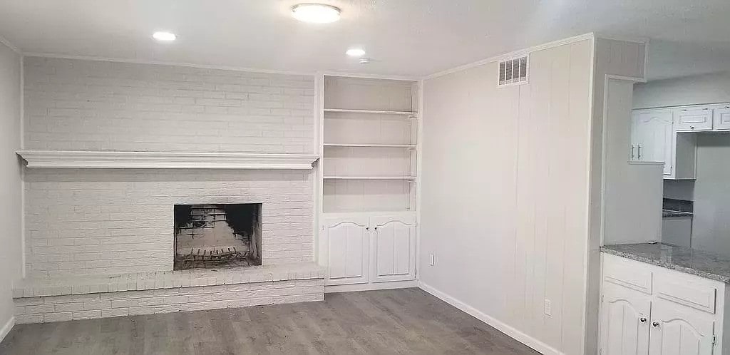 unfurnished living room with a brick fireplace, brick wall, and dark hardwood / wood-style floors