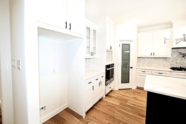 kitchen featuring stainless steel oven, white cabinets, light hardwood / wood-style flooring, gas stovetop, and tasteful backsplash