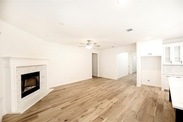 unfurnished living room with ceiling fan, a high end fireplace, and light wood-type flooring