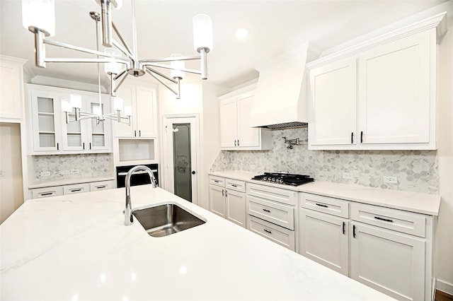 kitchen with white cabinetry, hanging light fixtures, sink, and custom exhaust hood