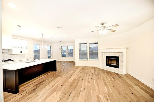 kitchen featuring sink, gas cooktop, white cabinetry, hanging light fixtures, and light wood-type flooring