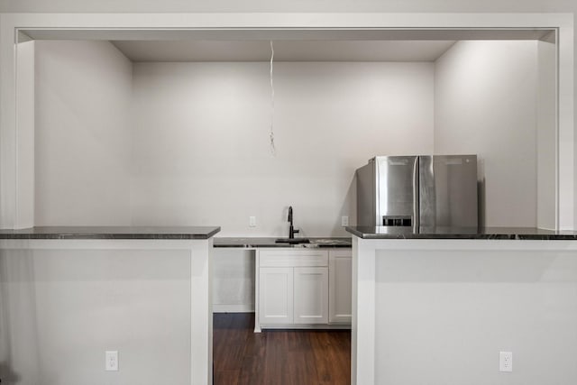 kitchen with dark wood-style flooring, a sink, white cabinetry, stainless steel refrigerator with ice dispenser, and dark countertops