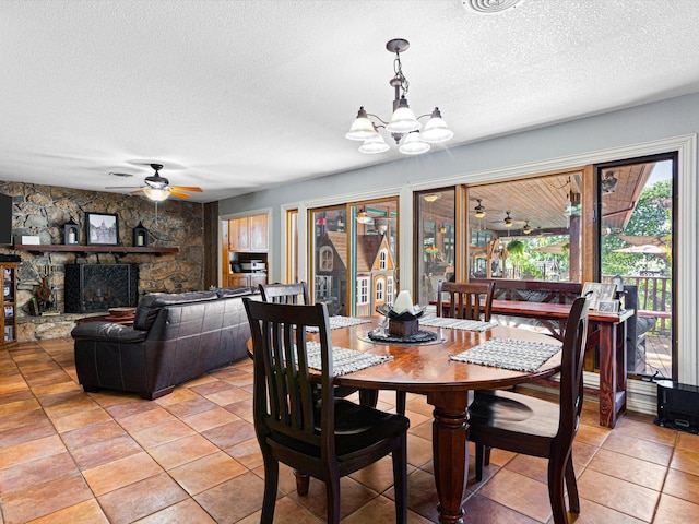 dining area featuring a textured ceiling, ceiling fan with notable chandelier, light tile patterned floors, and a fireplace