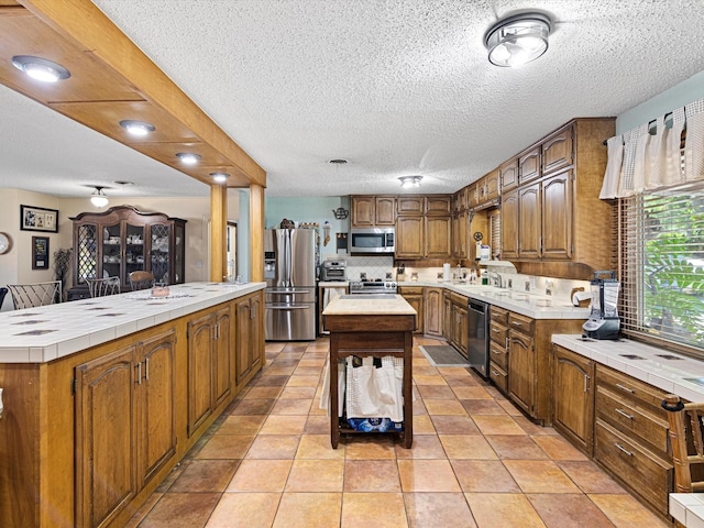 kitchen with a textured ceiling, a center island, stainless steel appliances, and light tile patterned floors