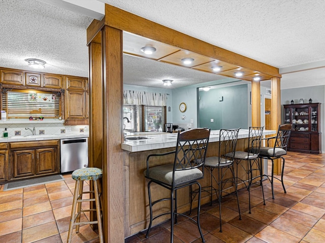 kitchen featuring a kitchen breakfast bar, dishwasher, a textured ceiling, and sink