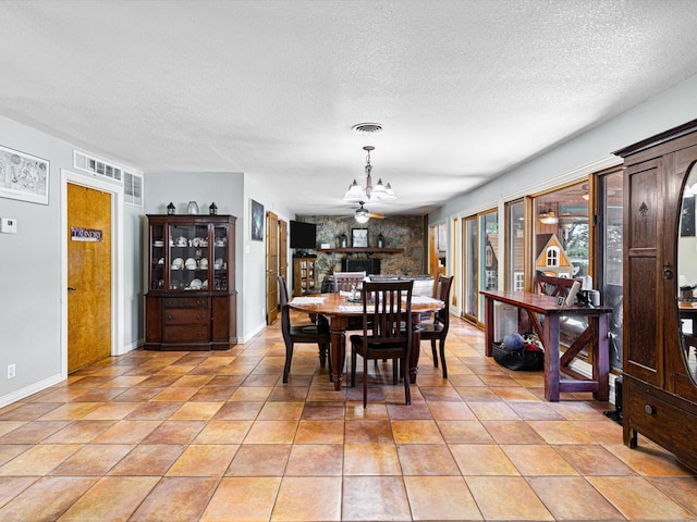 dining room with ceiling fan with notable chandelier, light tile patterned flooring, a stone fireplace, and a textured ceiling