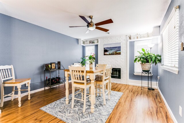 dining room with a brick fireplace, brick wall, hardwood / wood-style floors, and ceiling fan