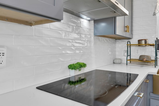 kitchen featuring gray cabinetry, decorative backsplash, wall chimney exhaust hood, and black electric cooktop