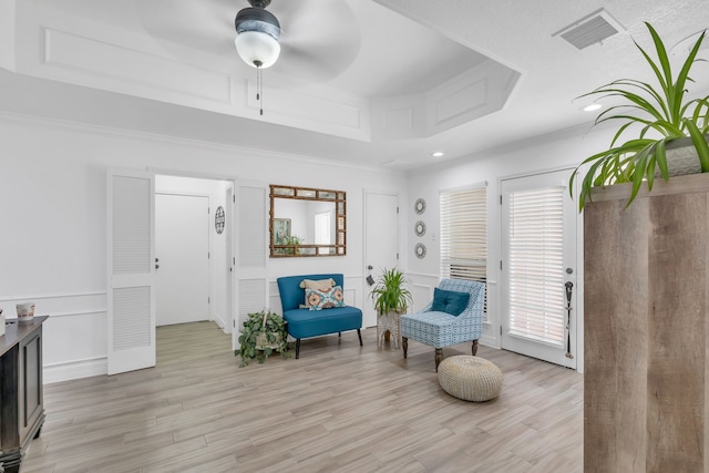 living area with ceiling fan, a tray ceiling, and light hardwood / wood-style floors