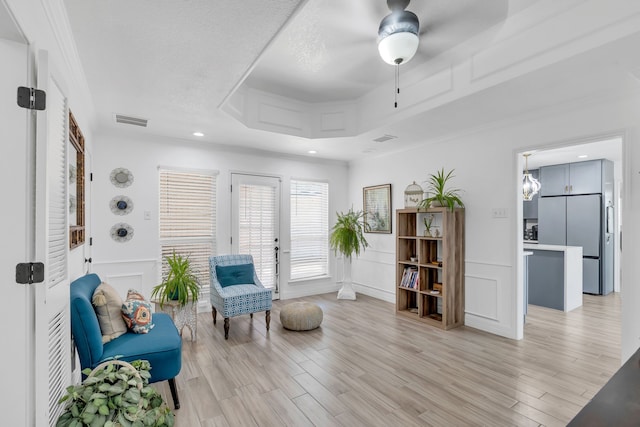 sitting room with ceiling fan, crown molding, light hardwood / wood-style flooring, and a tray ceiling