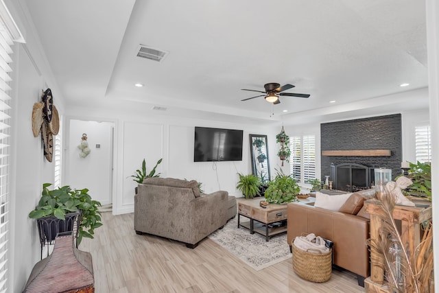 living room featuring ceiling fan, a fireplace, a raised ceiling, and light hardwood / wood-style floors