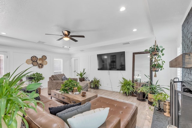 living room featuring a raised ceiling, ceiling fan, and light hardwood / wood-style floors