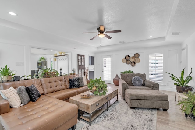 living room with light hardwood / wood-style flooring, ceiling fan, and a raised ceiling