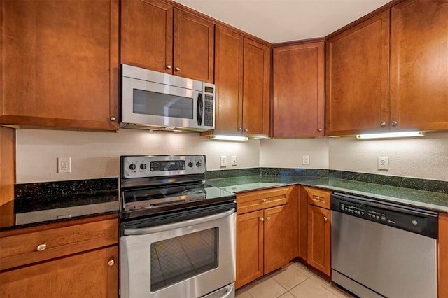 kitchen with appliances with stainless steel finishes, light tile patterned floors, and dark stone countertops