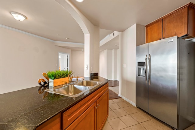 kitchen with crown molding, stainless steel fridge with ice dispenser, dark stone countertops, light tile patterned floors, and sink