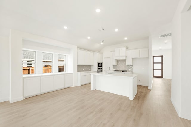 kitchen featuring built in microwave, light hardwood / wood-style floors, white cabinets, a kitchen island with sink, and tasteful backsplash