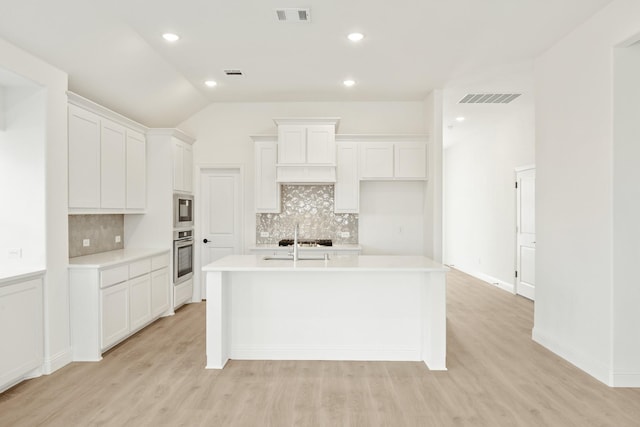 kitchen featuring an island with sink, built in microwave, white cabinets, and oven