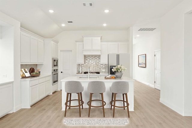 kitchen with a kitchen bar, white cabinetry, stainless steel appliances, and a kitchen island with sink