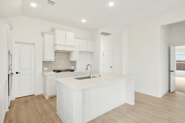 kitchen with sink, backsplash, stainless steel appliances, white cabinets, and an island with sink