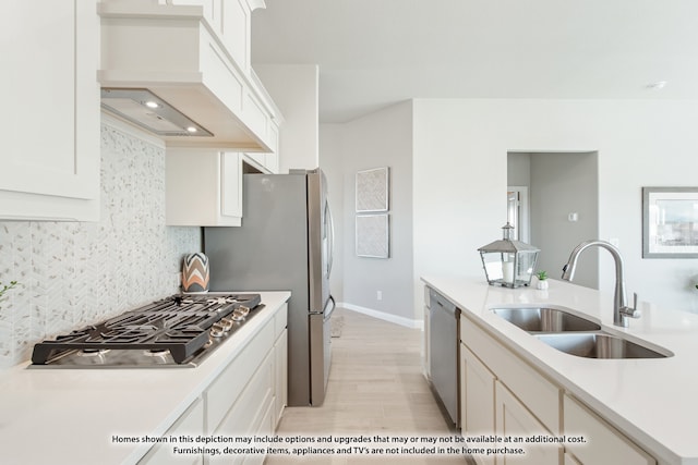 kitchen with custom exhaust hood, appliances with stainless steel finishes, white cabinets, light wood-type flooring, and sink