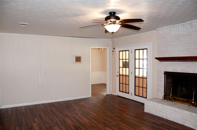 unfurnished living room with crown molding, a brick fireplace, french doors, ceiling fan, and dark wood-type flooring